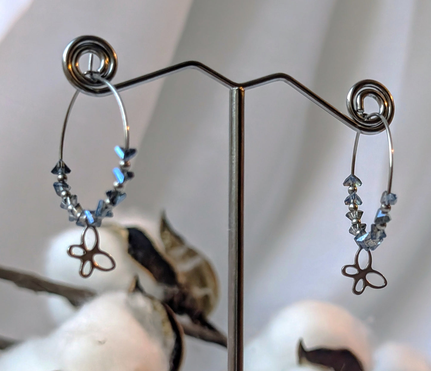 Vue floutée des Boucles d’oreilles Colombie en acier inoxydable, ornées d’un éclat de verre bleu-gris et d'un pendentif papillon