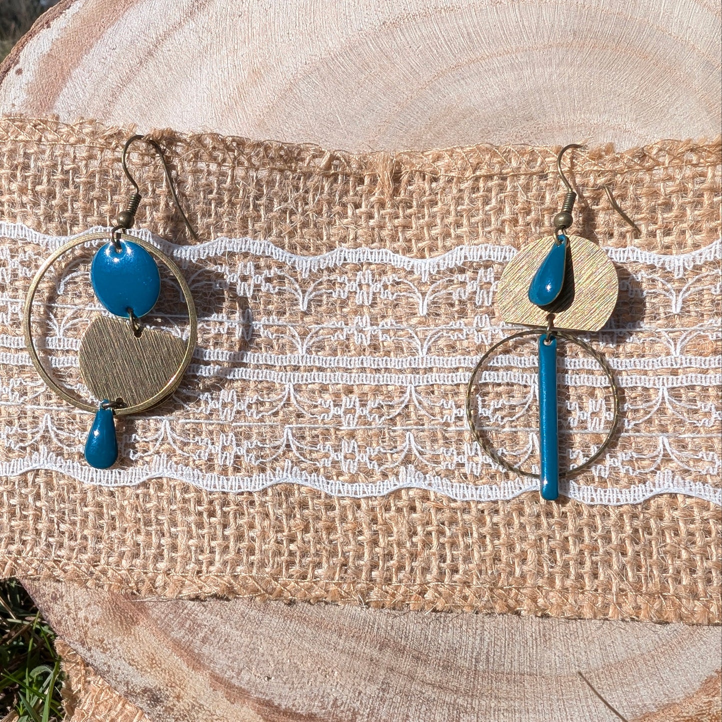 Boucles d'oreilles Vénus en laiton texturé bronze avec émaux bleu canard, présentées sur un fond en bois naturel.
