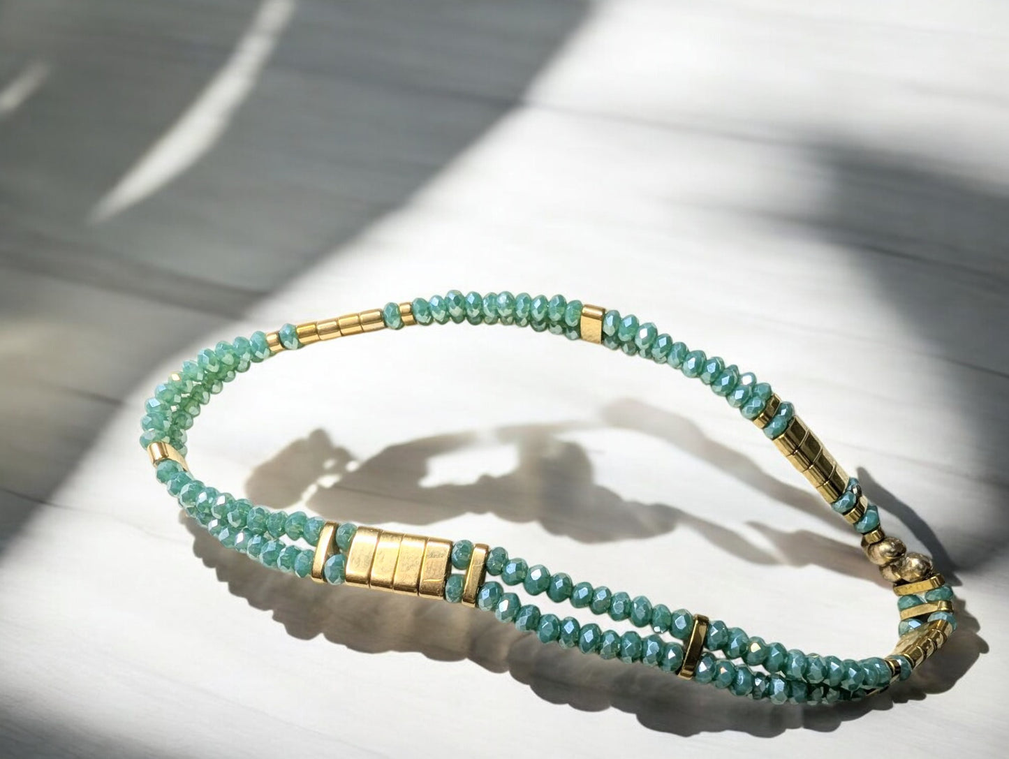 Bracelet Ondine en gros plan, mettant en valeur les perles de verre cyan irisé et les touches dorées d’hématite.