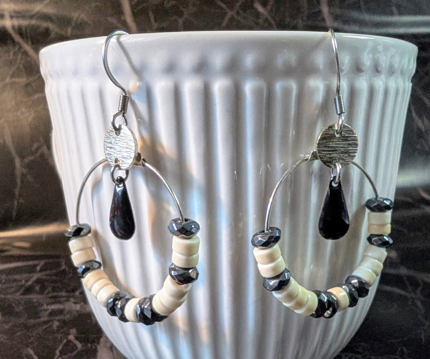 zoom sur les Boucles d'oreilles Céleste en acier inoxydable, avec perles d’howlite ivoire et hématite grise sur un cercle argenté.