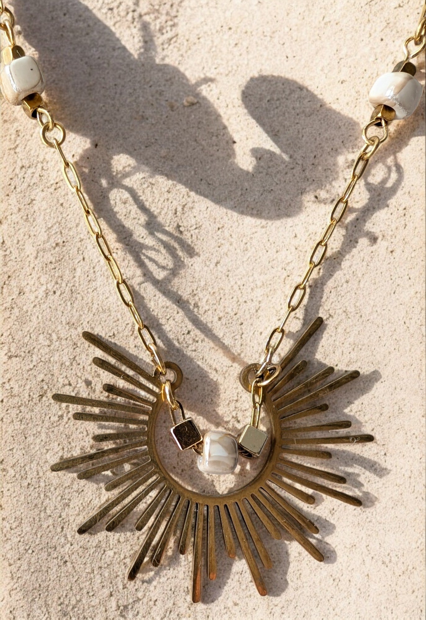 Gros plan sur le pendentif du collier Soléa, capturant l’éclat du soleil dans un bijou unique.