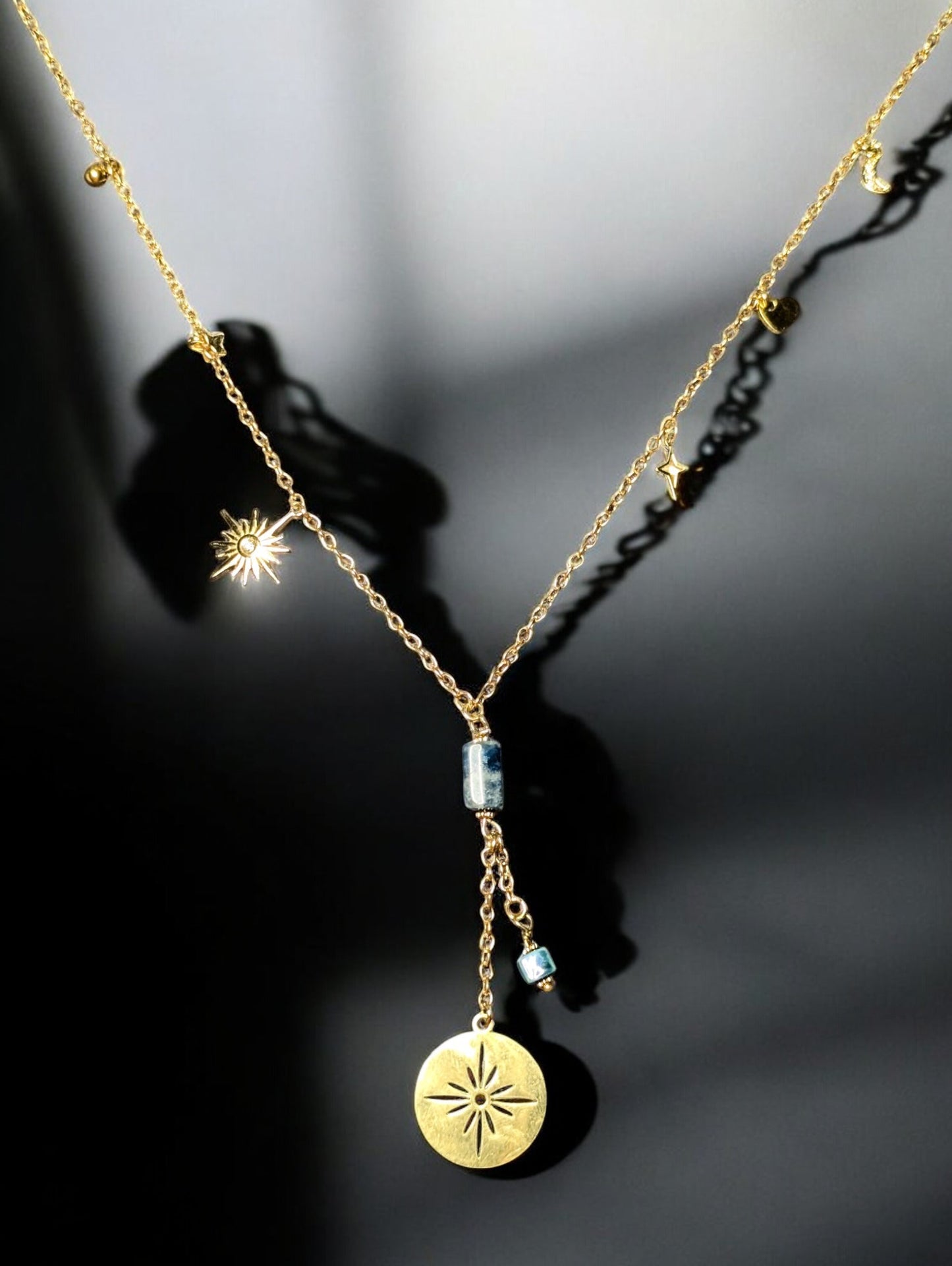 Collier sautoir Constellation en acier inoxydable doré, orné de breloques soleil, lune et étoiles avec une pierre d’apatite naturelle. zoom sur l'apatite et les breloques