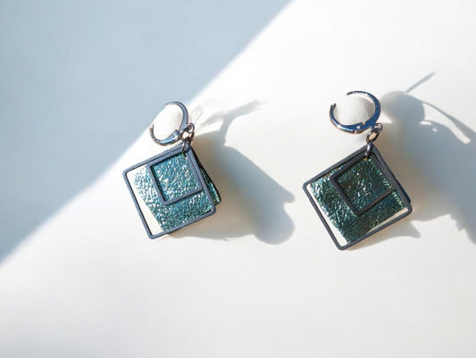 Boucles d'oreilles Emeraude en cuir vert texturé et acier inoxydable, avec un design minimaliste et moderne.