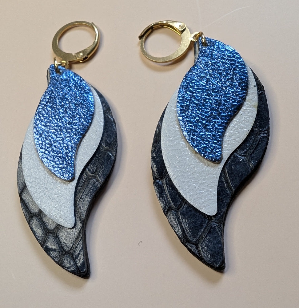 Boucles d'oreilles en cuir Version bleu nuit, blanc et bleu métallique de la collection Alaya, design élégant et intemporel, mis en valeur sur un fond simple pour souligner sa beauté et son raffinement.