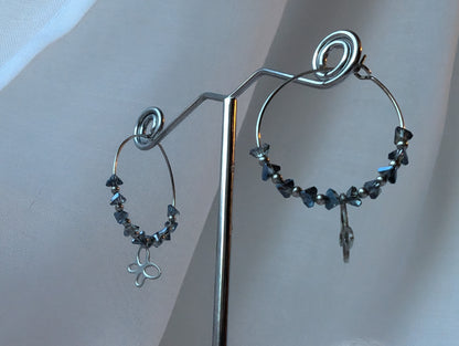 "Vue de profil Boucles d’oreilles Colombie en acier inoxydable, ornées d’un éclat de verre bleu-gris et d'un pendentif papillon. Un bijou élégant et raffiné, aux nuances délicates."