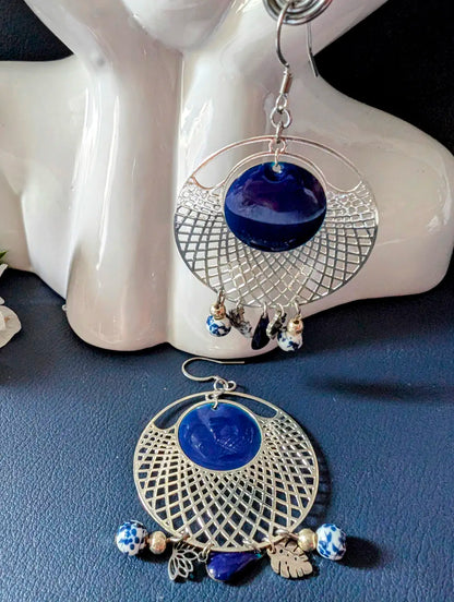Mise en scène des boucles pendantes Jardin d’Azur ornées de motifs floraux en céramique et de sequins émaillés bleu azur.