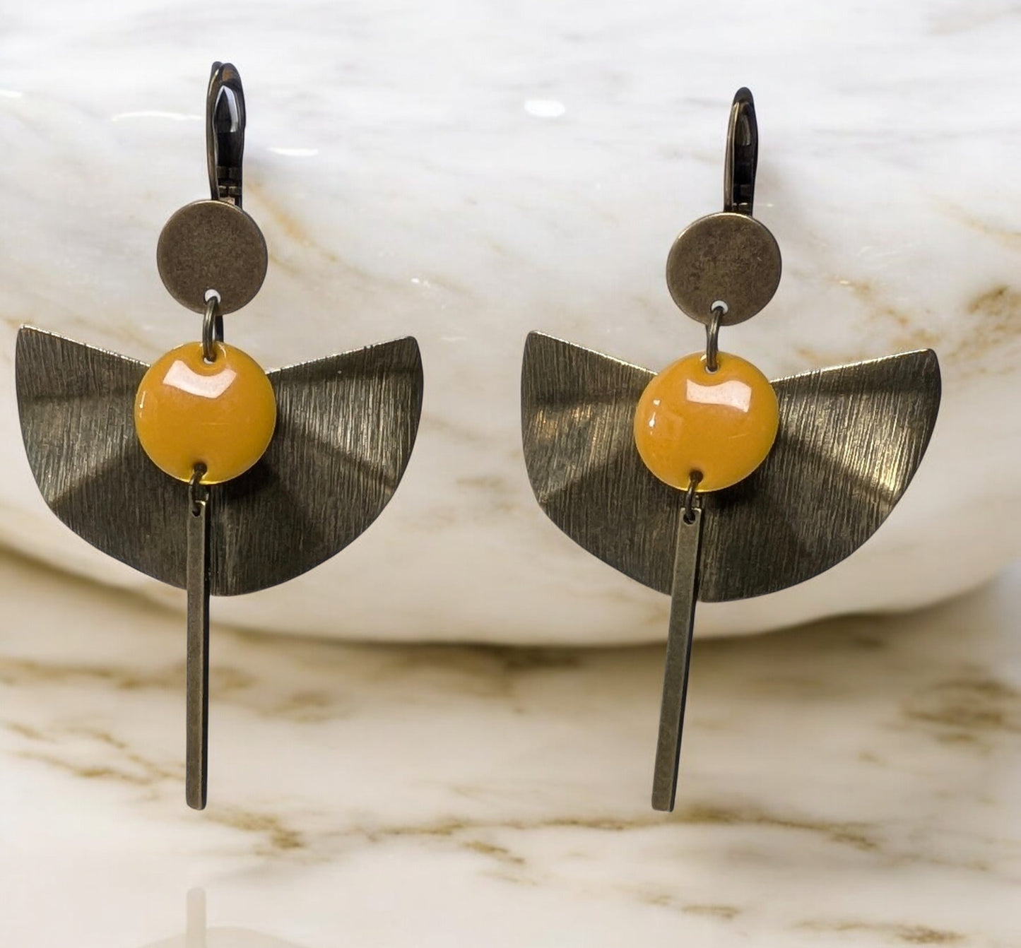 Boucles d’oreilles Zéphir en laiton bronze texturé avec un sequin émaillé orange, design en éventail et tige allongée. Bijou artisanal élégant et léger, idéal pour une touche estivale raffinée.