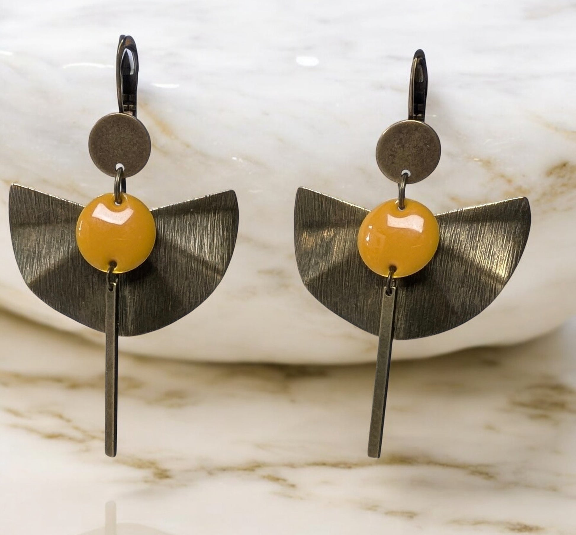 Boucles d’oreilles Zéphir en laiton bronze texturé avec un sequin émaillé orange, design en éventail et tige allongée. Bijou artisanal élégant et léger, idéal pour une touche estivale raffinée.