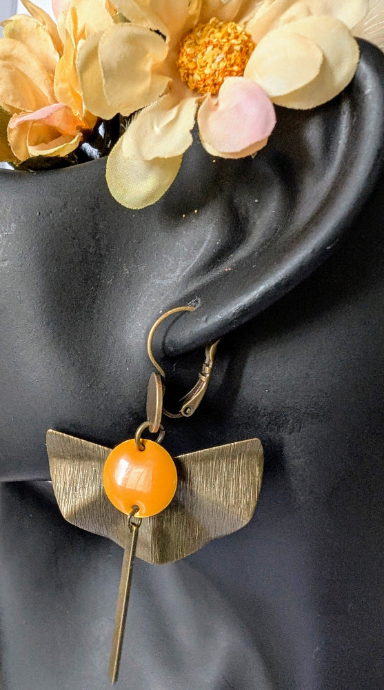 "Boucle d’oreille Zéphir portée sur un présentoir buste : laiton bronze texturé en éventail, sequin émaillé orange et tige allongée. Bijou artisanal élégant et raffiné, parfait pour un look estival