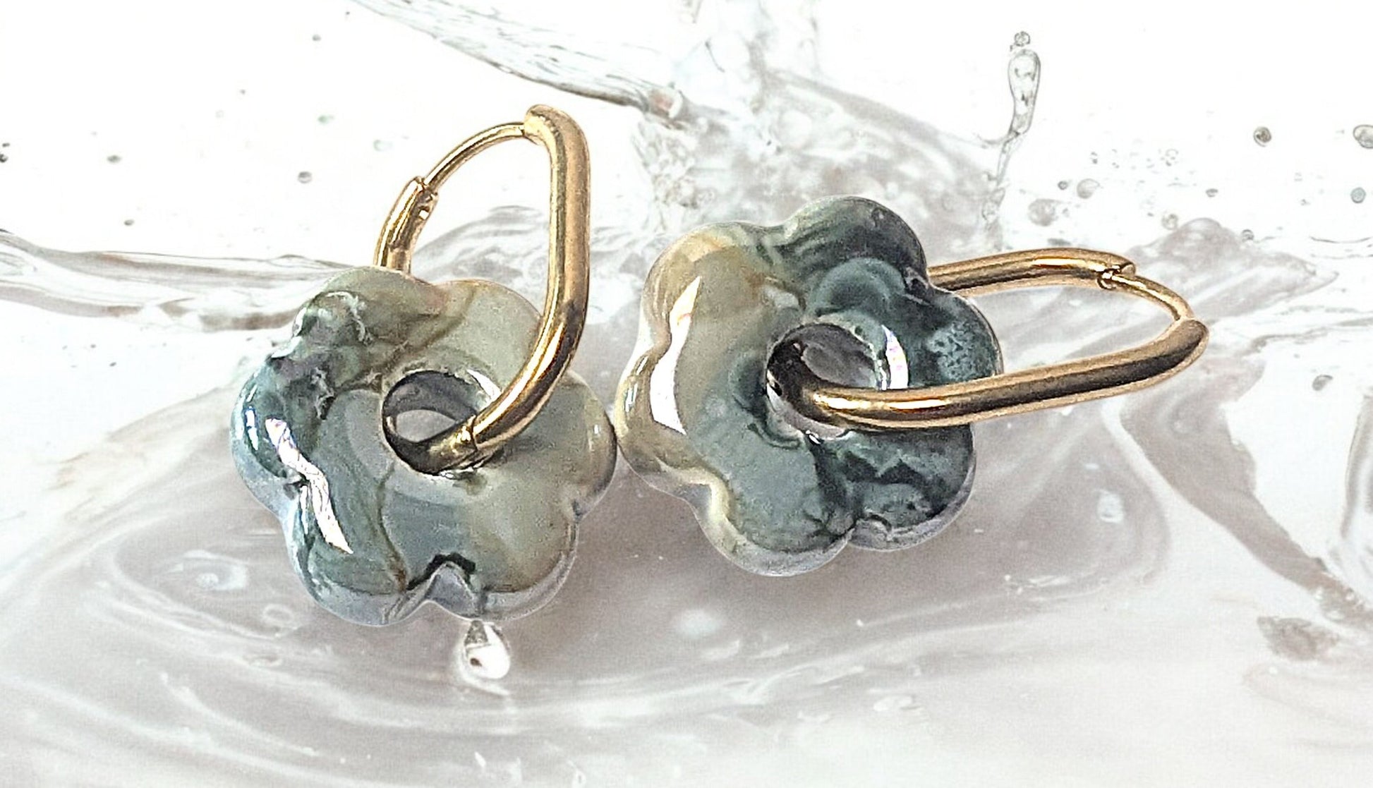 Gros plan sur une paire de boucles d’oreilles fleur en céramique bleu vert avec créoles dorées