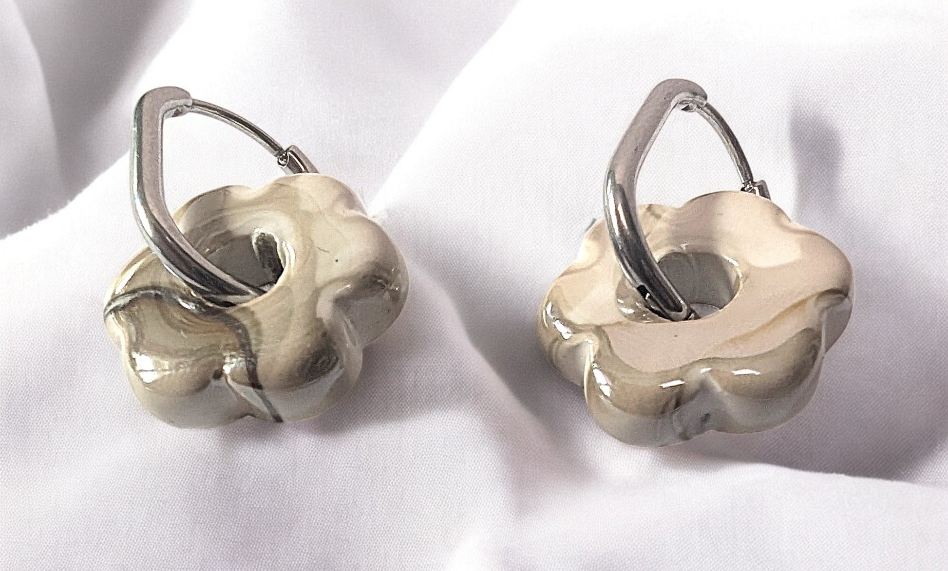 Gros plan sur une paire de boucles d’oreilles fleur en céramique greige avec créoles argentées