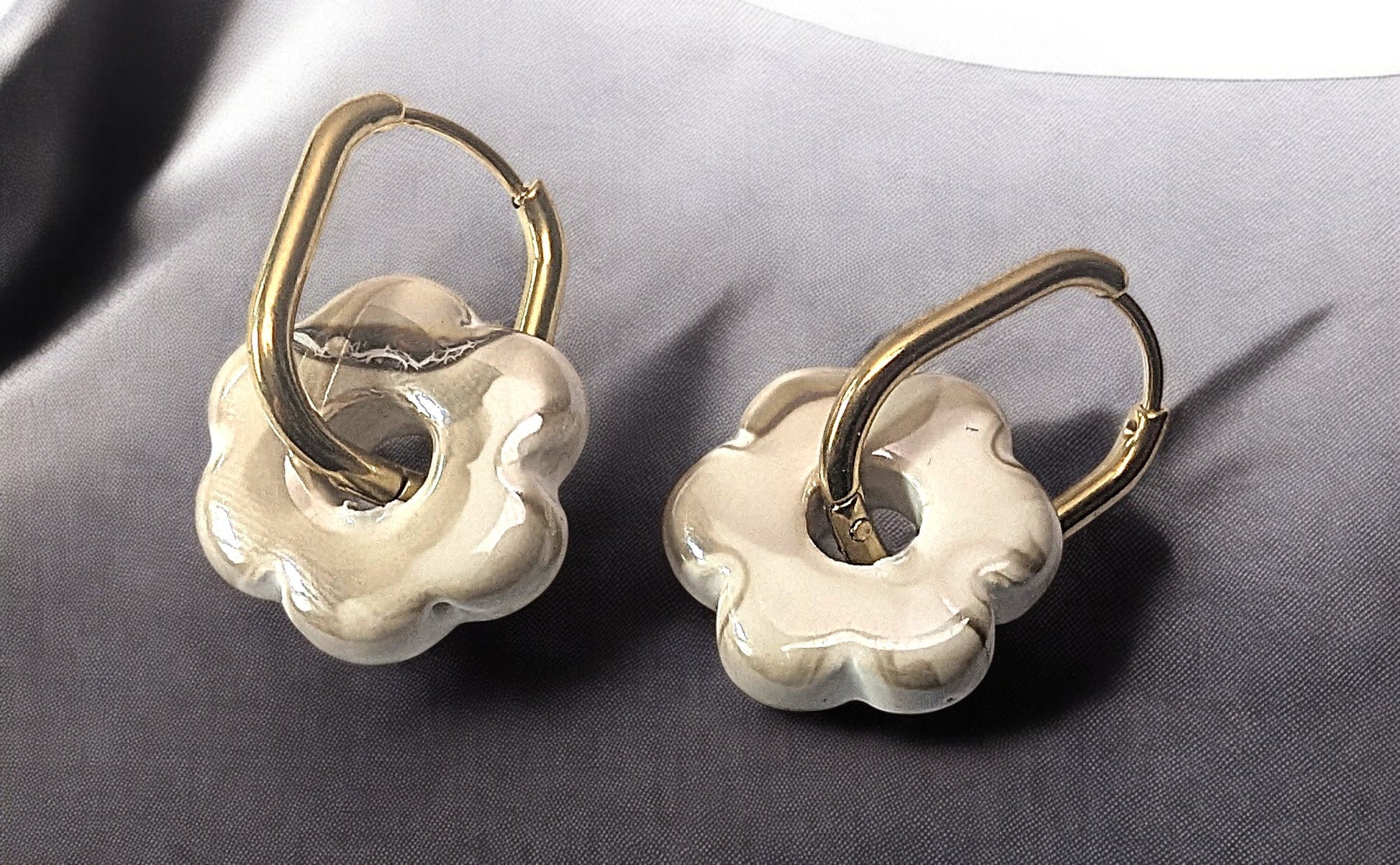 Gros plan sur une paire de boucles d’oreilles Fleur en céramique greige avec créoles dorées