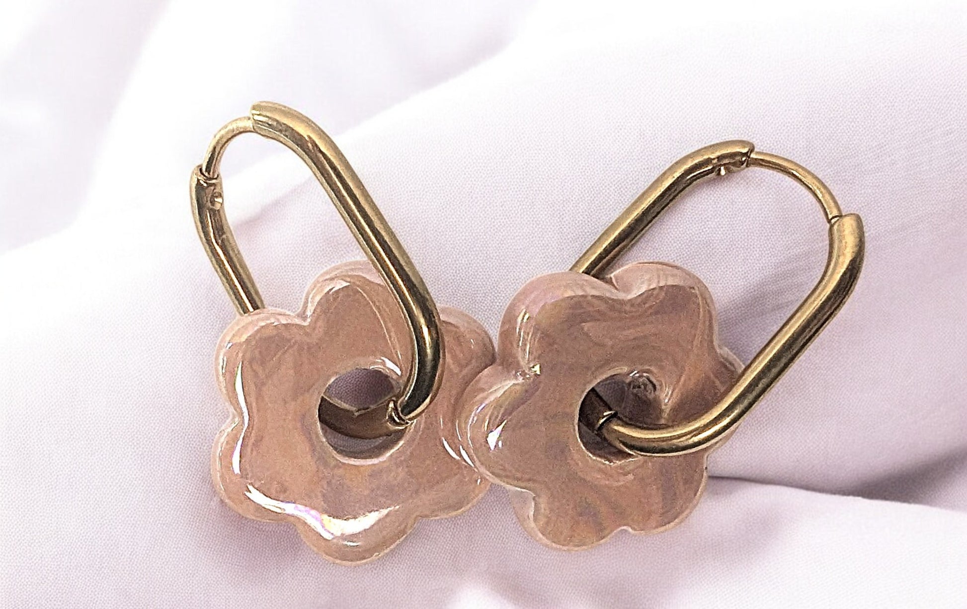 Gros plan sur une paire de boucles d’oreilles fleur en céramique rose clair avec créoles dorées. Le charme absolu. 