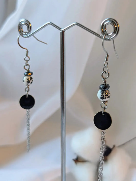 Boucles d’oreilles Pérébores noires en acier inoxydable avec connecteur émaillé noir, perles céramiques blanches et fleurs noires.
