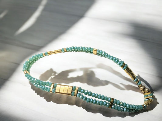Bracelet Ondine en gros plan, mettant en valeur les perles de verre cyan irisé et les touches dorées d’hématite.