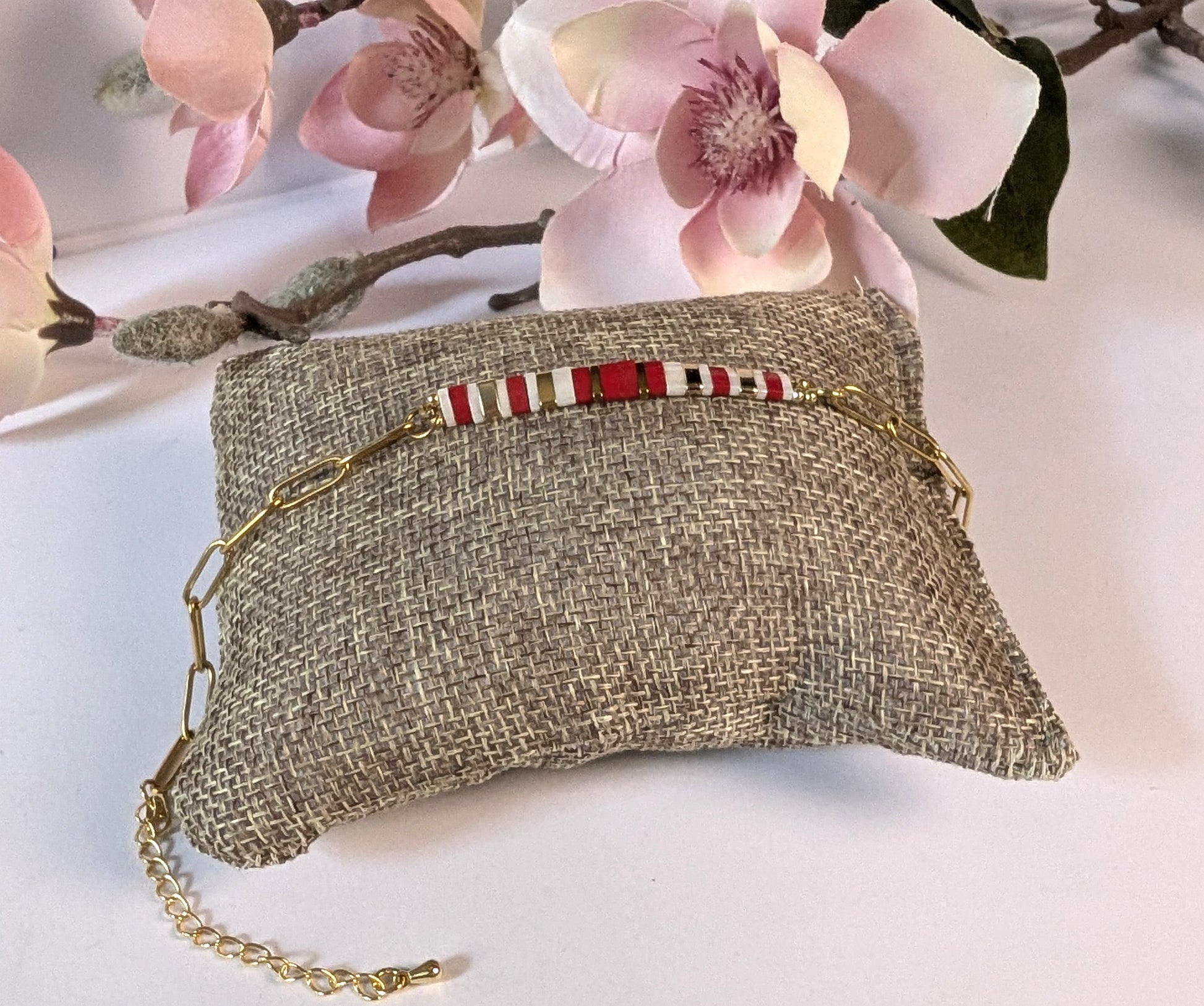 Détail de la chaîne trombone dorée du bracelet Rosso, élégante et moderne. Mise en scène sur petit coussin et fleurs.