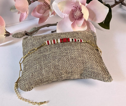 Détail de la chaîne trombone dorée du bracelet Rosso, élégante et moderne. Mise en scène sur petit coussin et fleurs.