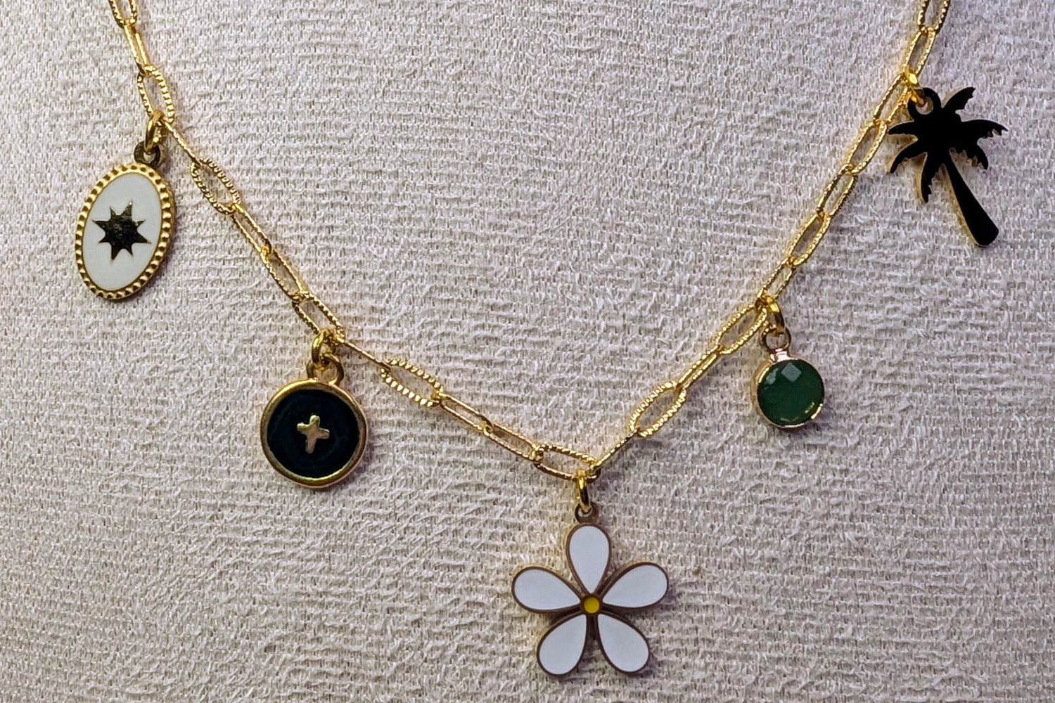 Détail des breloques du collier Liora : étoile du berger, croix verte, fleur, palmier