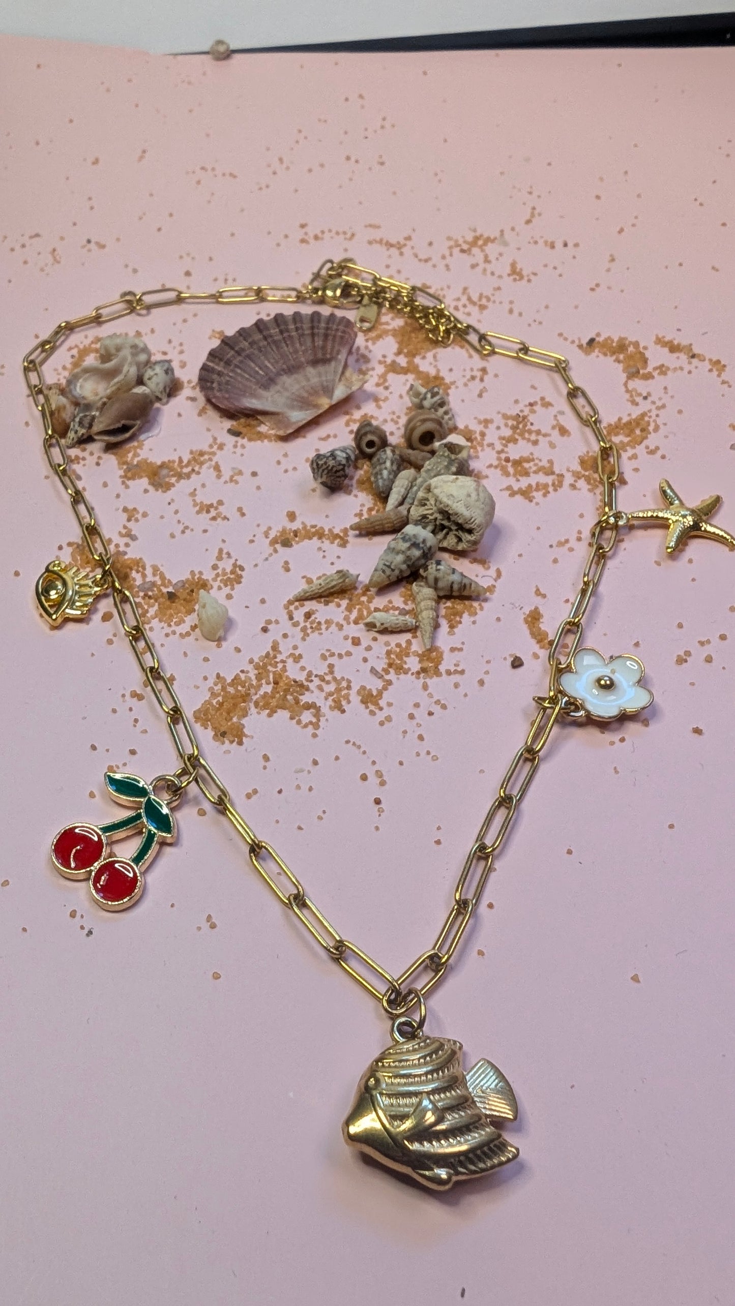 Collier Zélie avec charms colorés et symboliques sur chaîne dorée, dans décor de coquillages