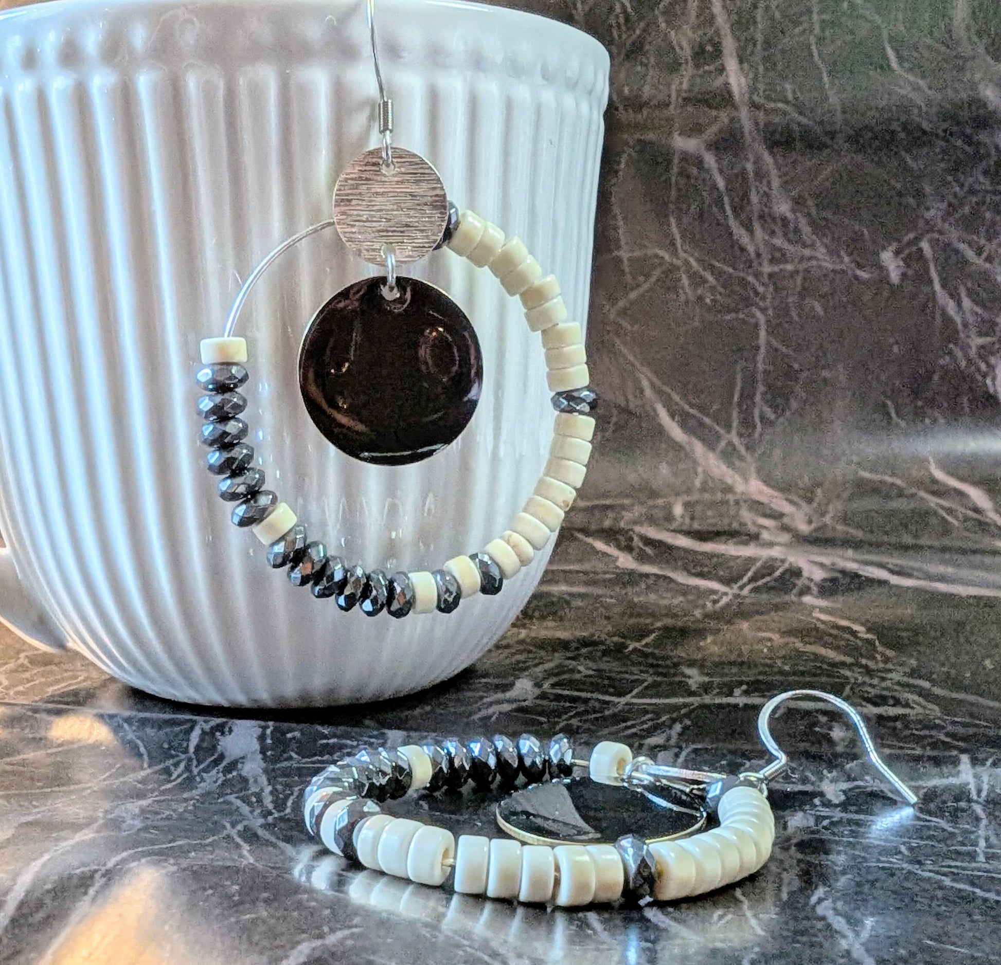 Boucles d’oreilles éclipse d'ivoire howlite et hématite, avec perles ivoire et métallisée montées sur un cercle en acier inoxydable. Photo sur marbre noir