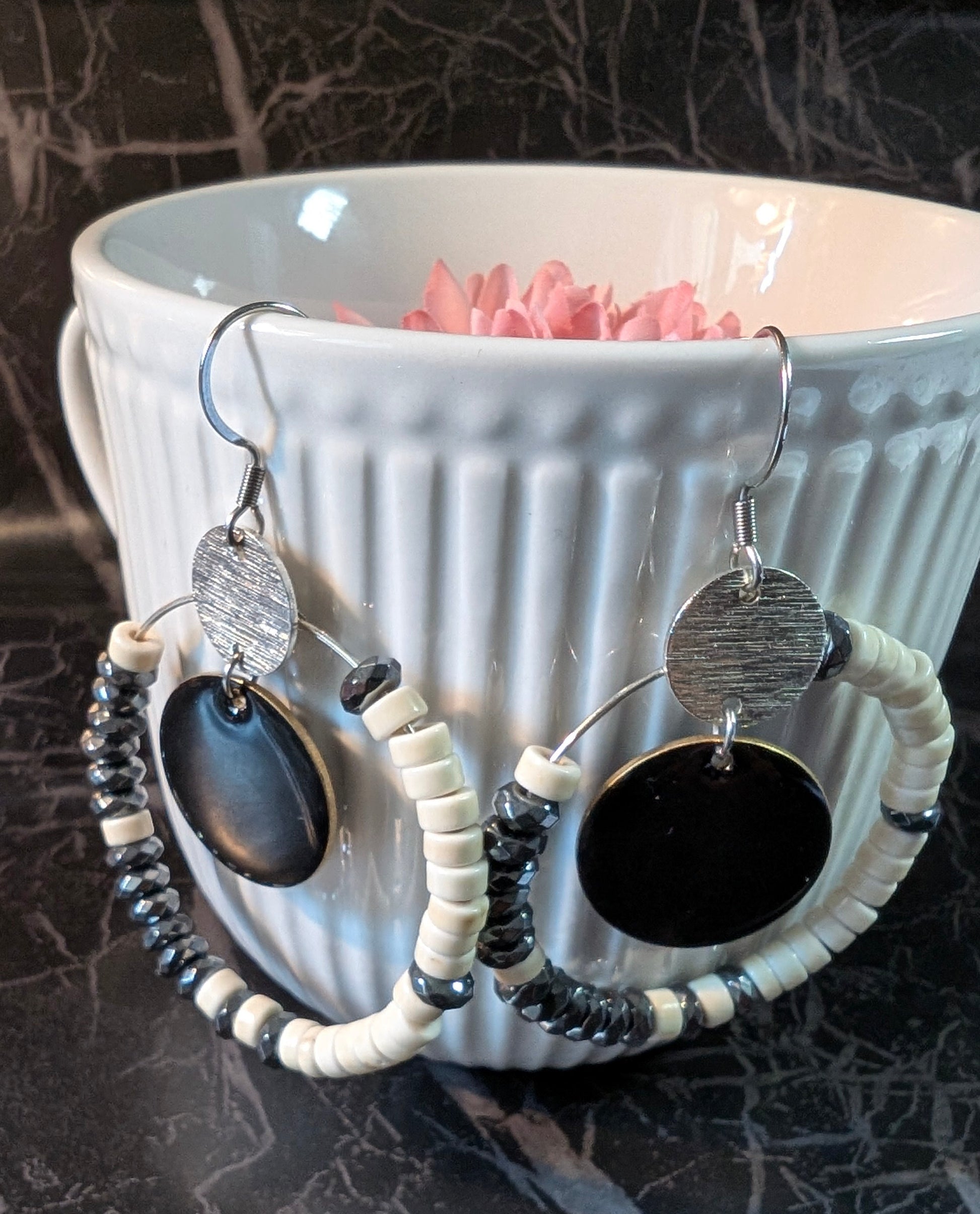 Boucles d’oreilles éclipse d'ivoire howlite et hématite, avec perles ivoire et métallisée montées sur un cercle en acier inoxydable. Ici photo des boucles accrochées a une tasse.