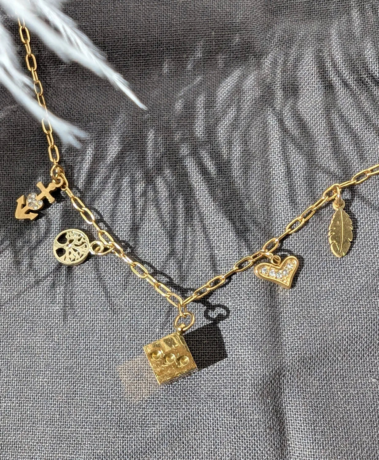 Détails des charms du collier Lyséa : dé argenté, plume délicate, croix de Camargue, arbre de vie et cœur scintillant en zirconium.