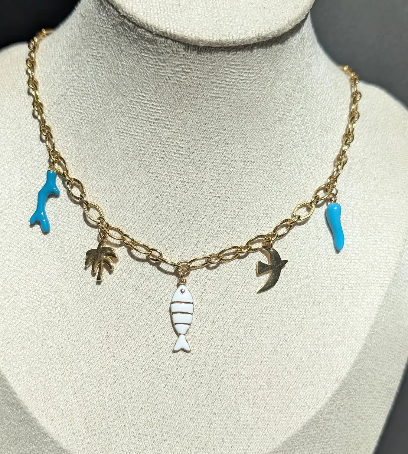 Collier Majorque avec charms tropicaux : corail turquoise, palmier doré, poisson blanc et doré, oiseau et corne d’abondance turquoise sur une chaîne ovale striée.