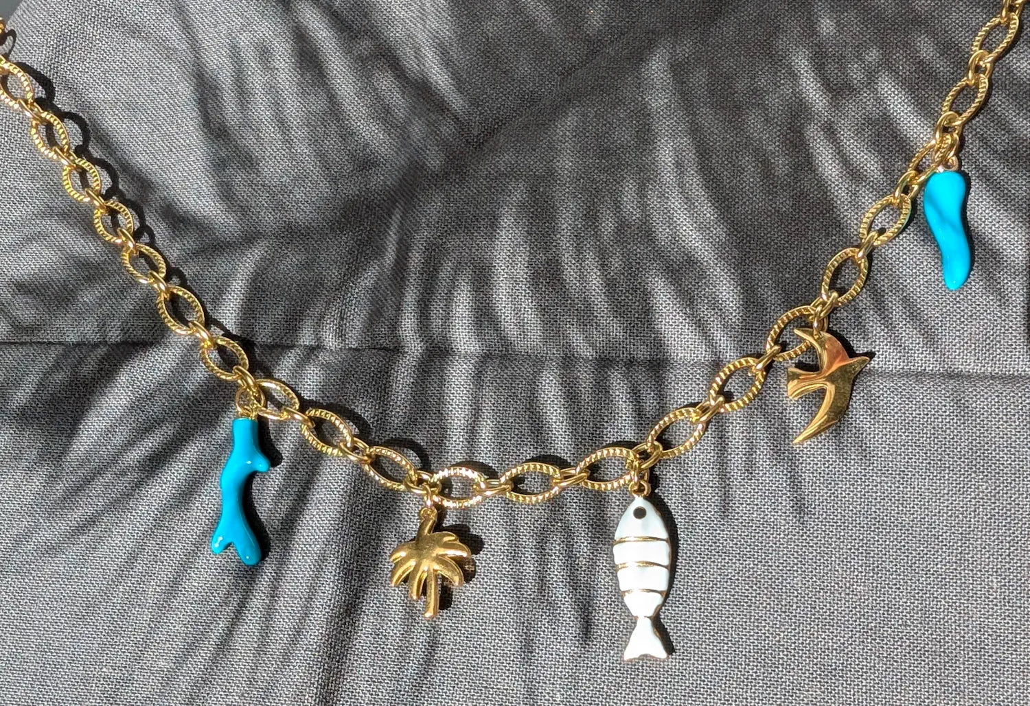 Détails des charms du collier Majorque : corail turquoise, palmier doré, poisson blanc et doré, oiseau et corne d’abondance turquoise.