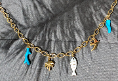 Détails des charms du collier Majorque : corail turquoise, palmier doré, poisson blanc et doré, oiseau et corne d’abondance turquoise.