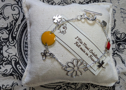 Gros plan sur le bracelet Floréale, mettant en valeur ses motifs floraux éclatants et son fermoir toggle en acier inoxydable. Mise en scène sur petit coussin et marque.