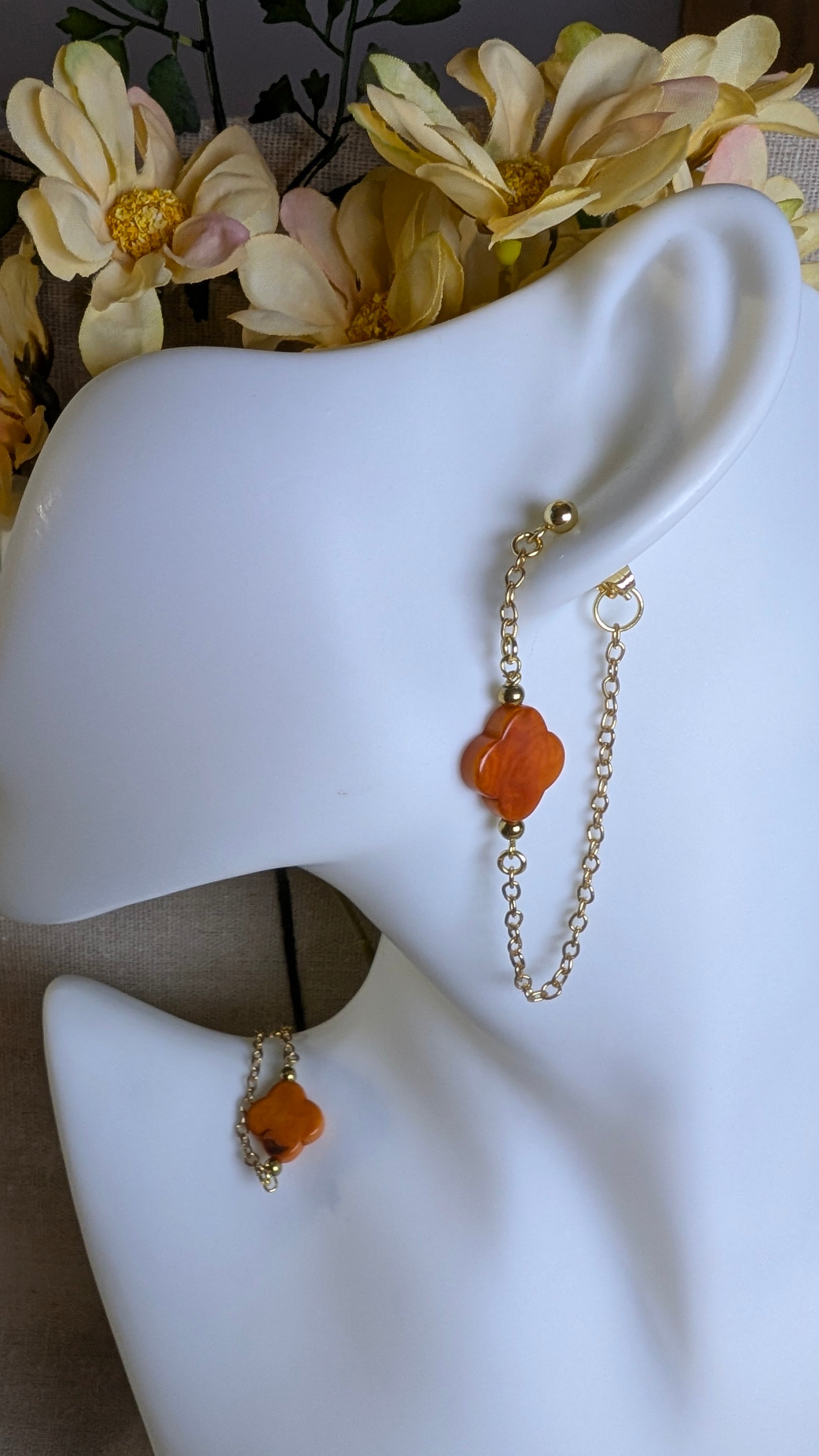 Boucles d’oreilles Cléa en acier inoxydable doré ou argenté, avec perle de Tagua en forme de trèfle et chaîne fine traversante pour un effet aérien. Ici perle orange et achaine dorée