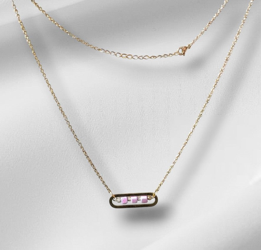 Collier Roséa en acier inoxydable doré avec perles cubes en céramique rose et perles métalliques ciselées, présenté à plat