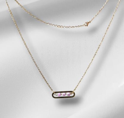 Collier Roséa en acier inoxydable doré avec perles cubes en céramique rose et perles métalliques ciselées, présenté à plat