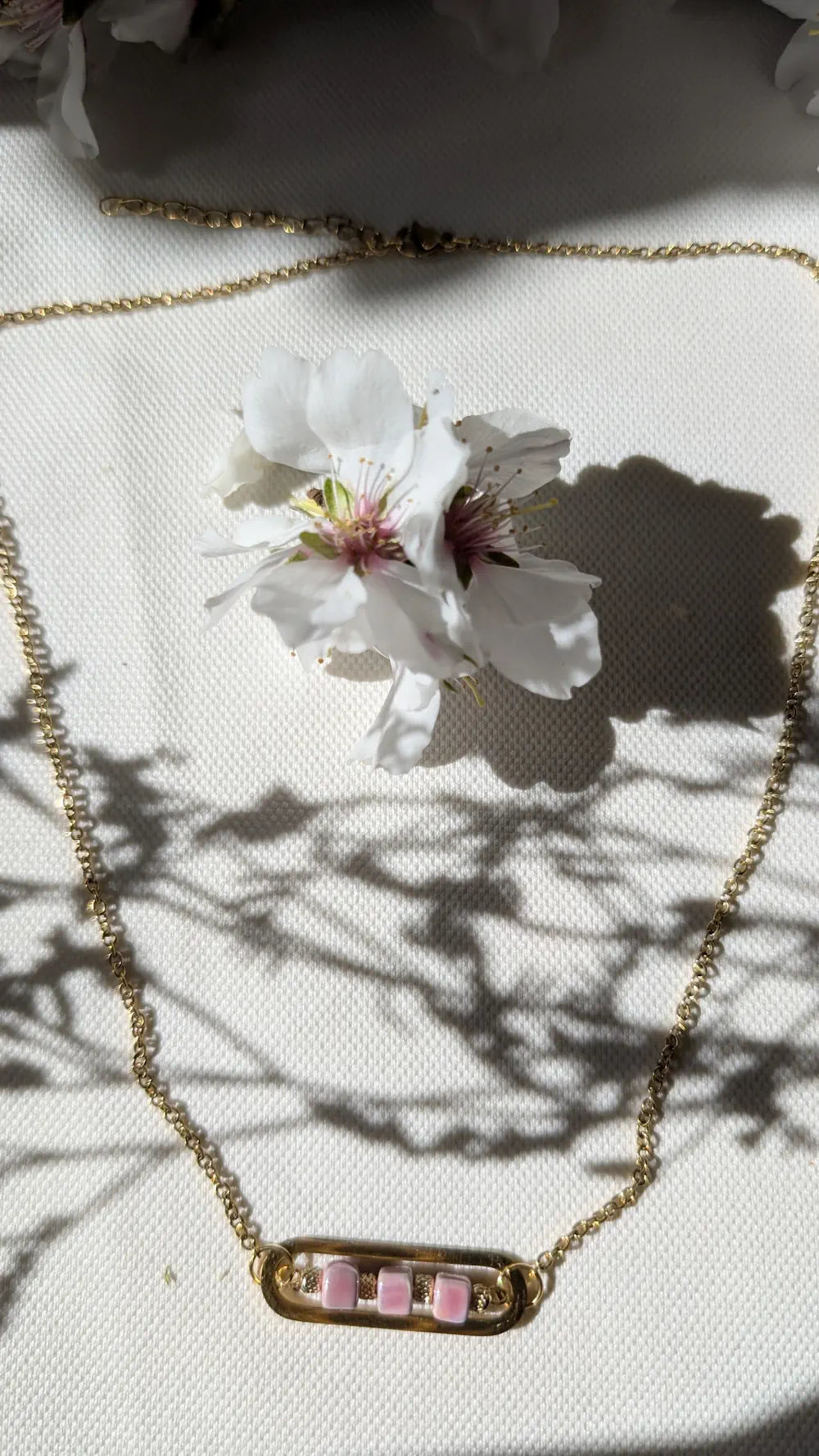 Collier Roséa avec chaîne dorée et perles en céramique rose, disposé en cercle sur un fond neutre pour sublimer son éclat.