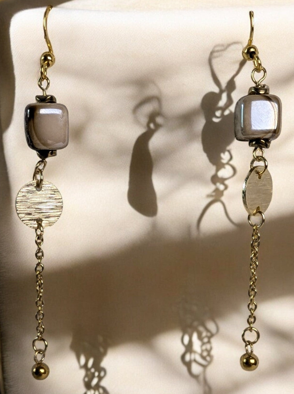 "Boucles d'oreilles Florentine, élégant design avec cubes en céramique et chaînette légère en acier inoxydable doré". Photo avec jeu d'ombre
